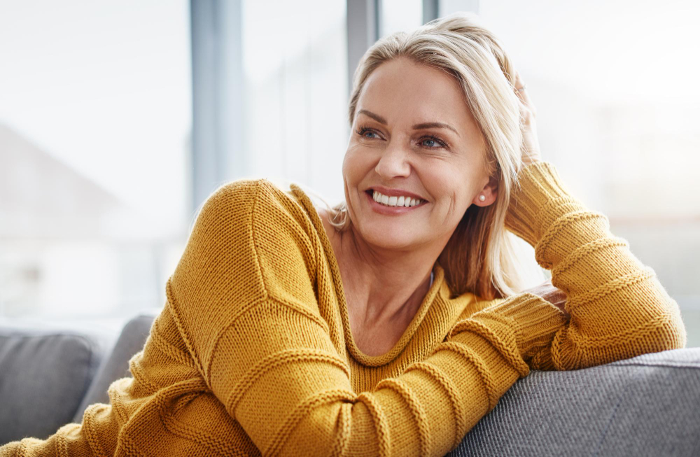 Smiling older woman wearing yellow sweater sitting on a couch.
