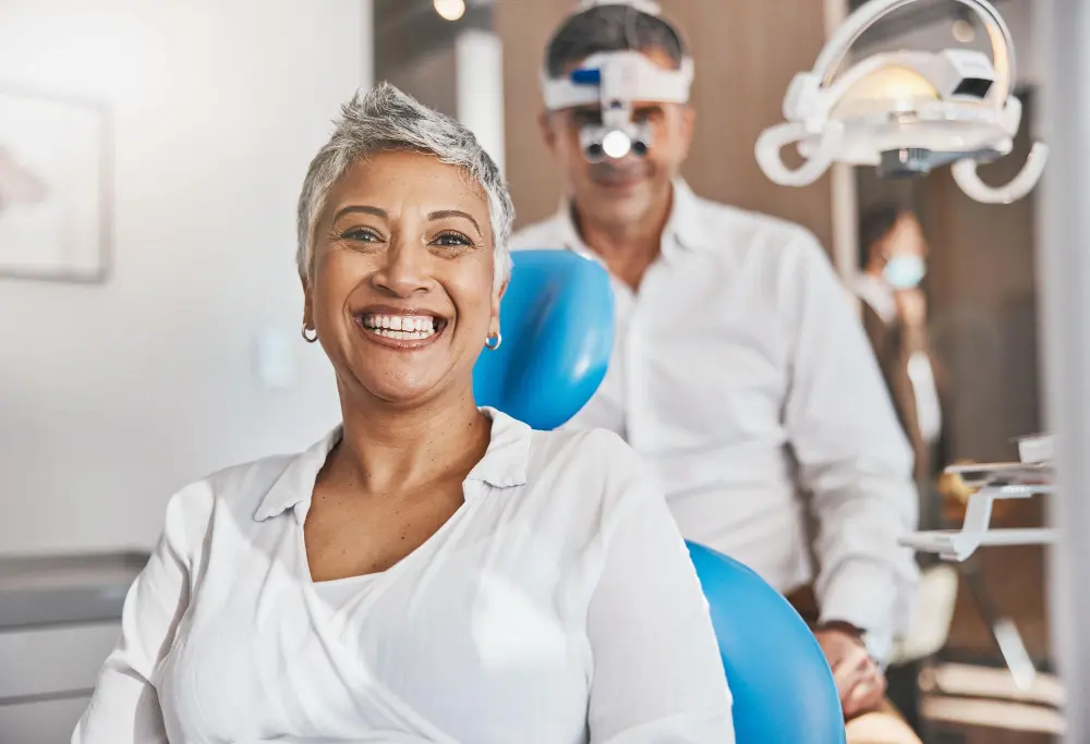Happy dental patient smiling while sitting in dental chair with dentist standing behind her.